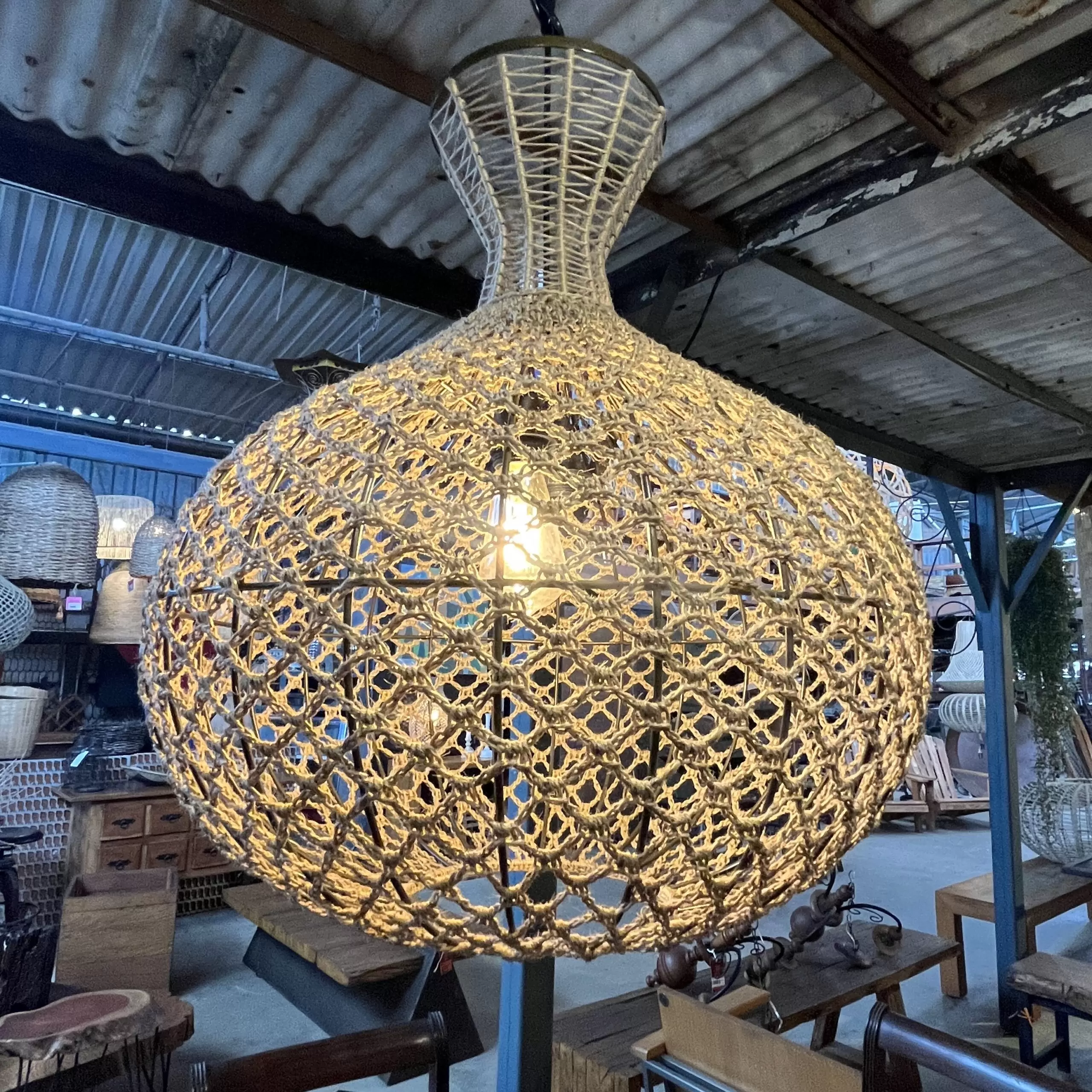 Luminária pendente artesanal feita de fibra natural trançada, criando um efeito de luz e sombra aconchegante para ambientes internos.