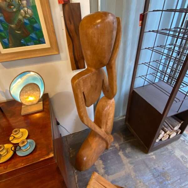 Escultura "O Pensador" em madeira rústica, representando figura humana em pose reflexiva.